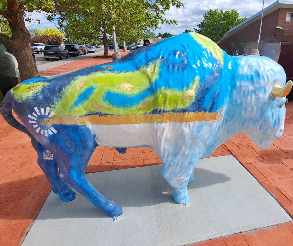 Buffalo Statue with green and blue painted on the top like an earth blanket with light blue and clouds like the sky on the rest of the body. The Chartway logo is painted on the side. 